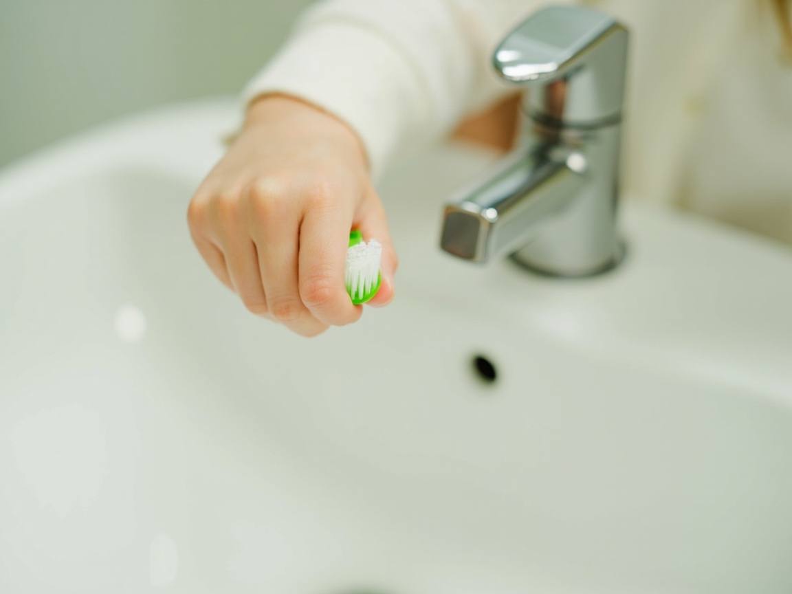 Main d’enfant tenant une brosse à dents verte au-dessus d’un lavabo blanc
